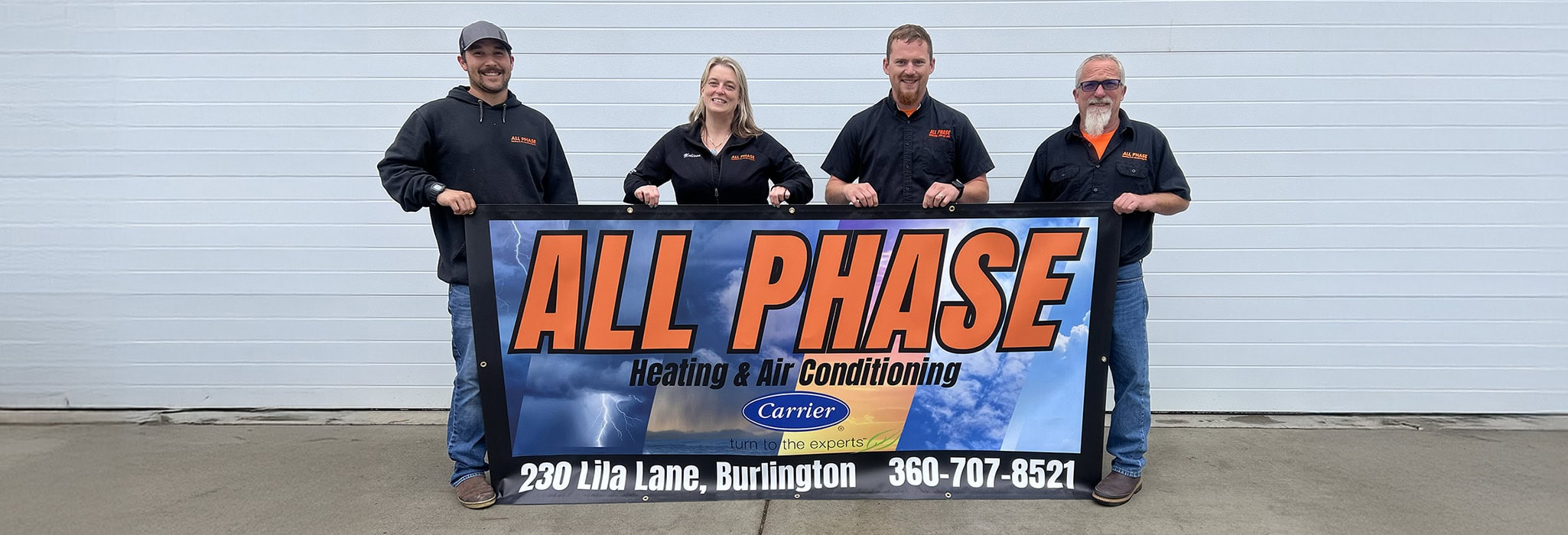 The All Phase team standing together outside their office in Burlington, WA holding a company banner.