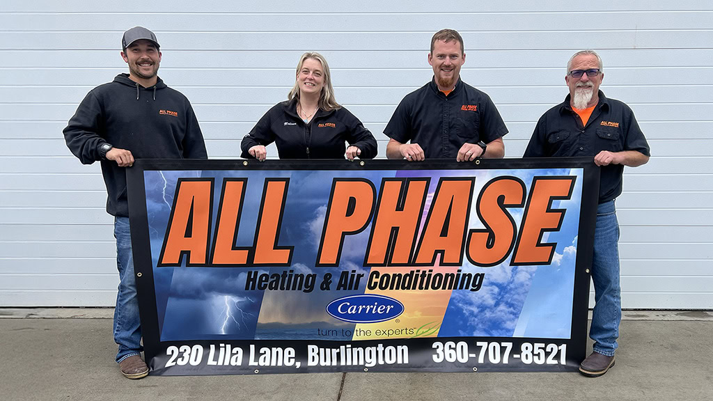 The All Phase team standing together outside their office in Burlington, WA holding a company banner.